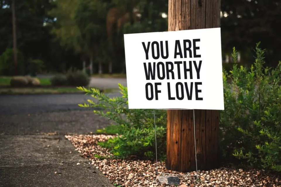 A sign on a wooden post reads: You are worthy of love